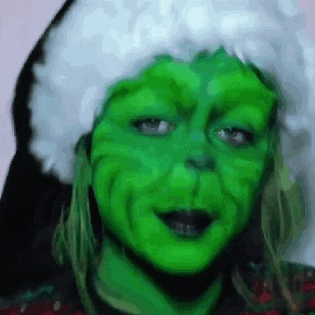 a close up of a person 's face with green paint and a santa hat on .