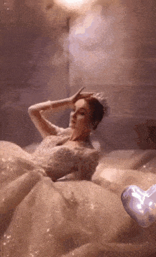 a woman in a wedding dress is laying on a bed with her hands on her head