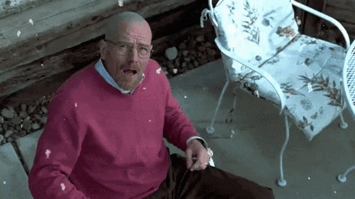 a man in a pink sweater and glasses is sitting in a chair with a chair in the background .