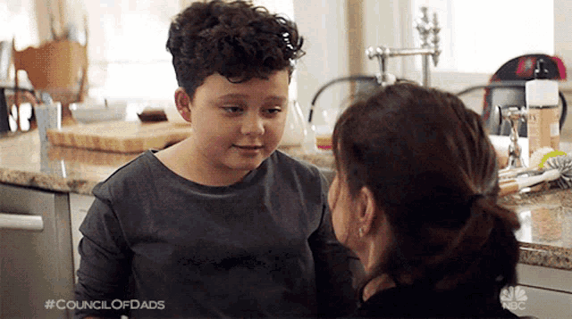 a woman and a young boy are looking at each other in a kitchen .