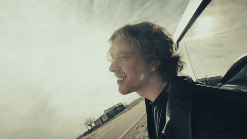 a man with curly hair is smiling and looking out the window of a car