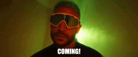 a man wearing sunglasses is standing in front of a green light and says `` coming ! ''
