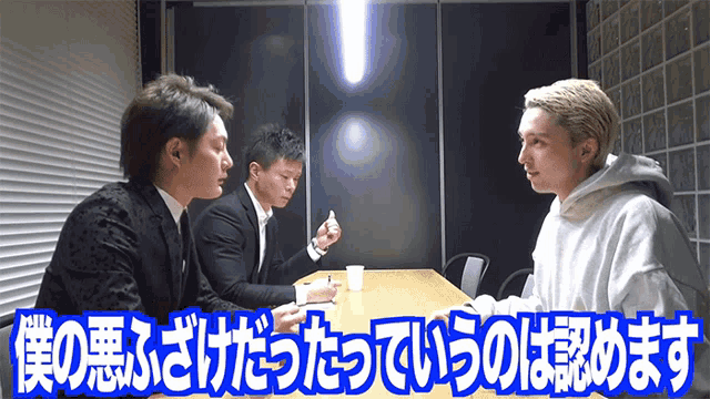 three men are sitting at a table in a room with chinese writing on it