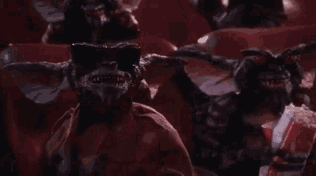a group of gremlins are sitting in a theatre eating popcorn .
