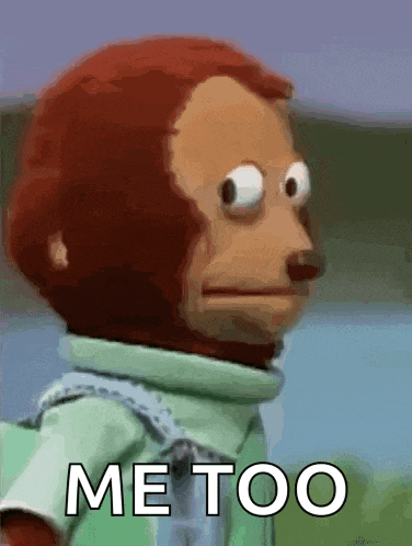 a stuffed monkey with big eyes is standing in front of a sign that says me too .