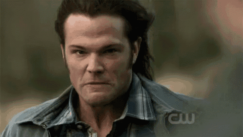 a man with long hair and a plaid shirt is making a serious face .