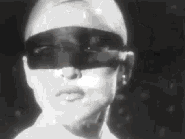 a black and white photo of a woman wearing sunglasses and a mask .
