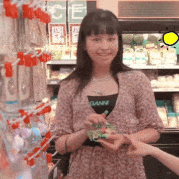a woman wearing a ganni shirt is holding a green object in her hand
