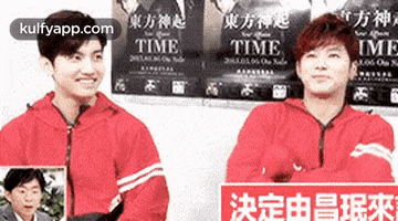 two men in red jackets are standing next to each other in front of a wall with posters for time .