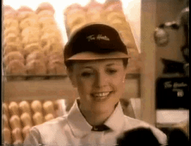 a woman wearing a tim hortons hat smiles in front of a display of donuts