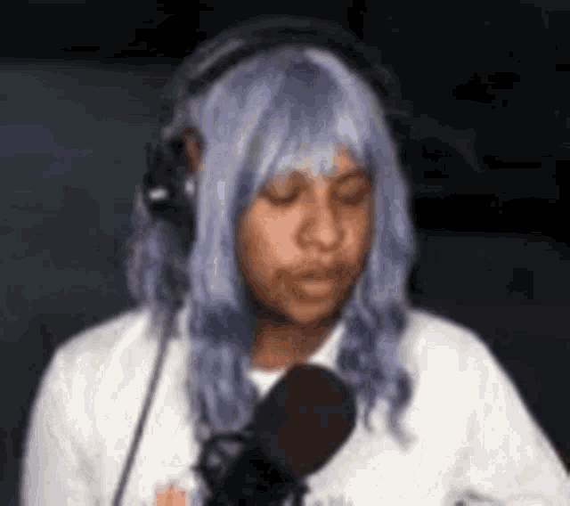 a woman wearing a purple wig and headphones is talking into a microphone .