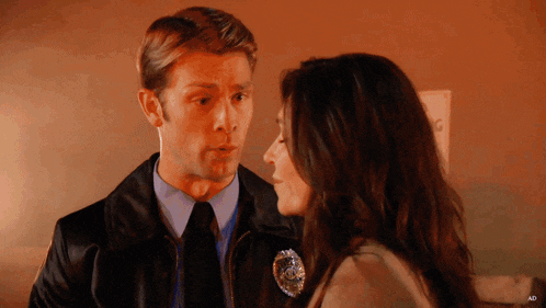 a man in a leather jacket talks to a woman with a badge on her shoulder