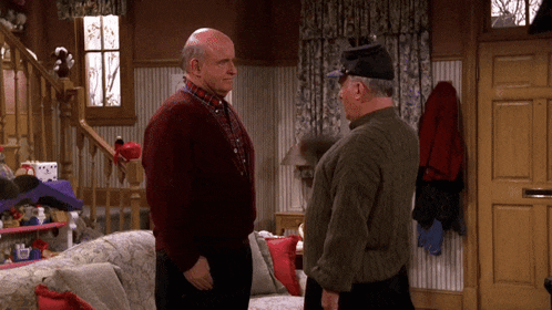 two men standing next to each other in a living room talking