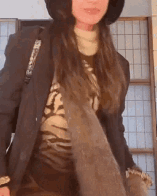 a woman wearing a hat and a jacket is standing in front of a wall .