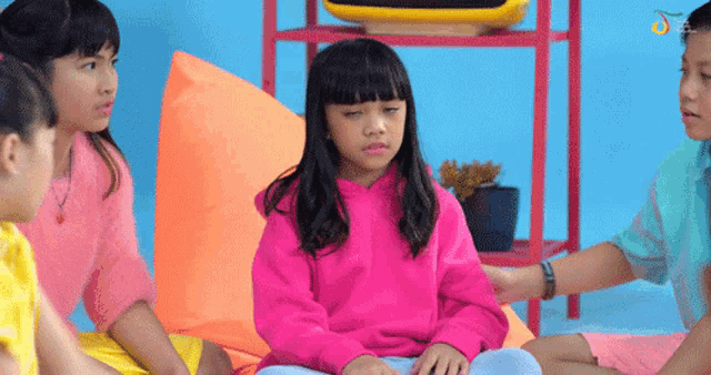 a girl in a pink sweatshirt is sitting on a bean bag chair with other children
