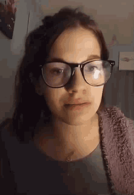 a young girl wearing glasses and a purple sweater looks at the camera