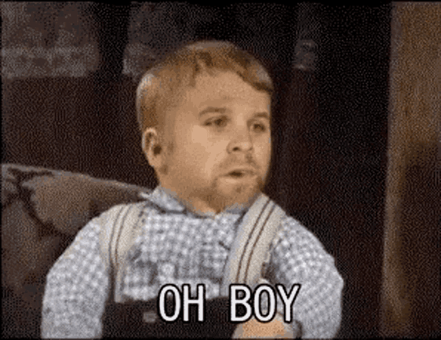 a little boy with a beard and suspenders is sitting on a couch .
