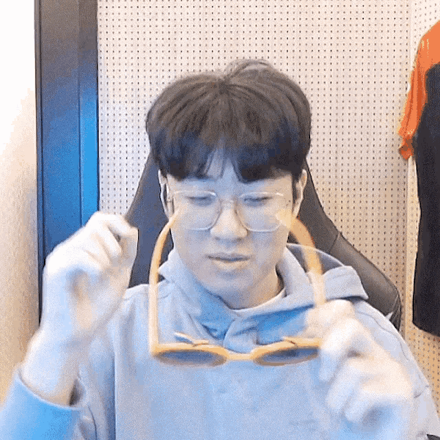 a young man wearing glasses and a hoodie is holding a pair of sunglasses in his hands