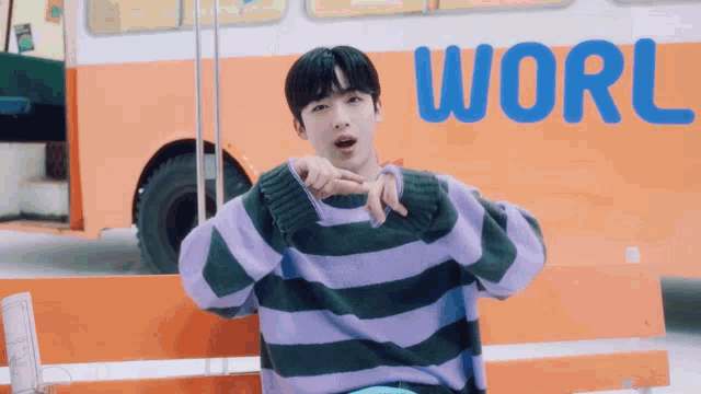 a man wearing a purple and green striped sweater is standing in front of an orange bus that says world