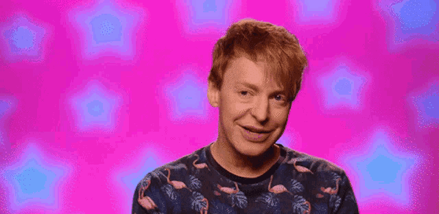 a man with red hair is wearing a flamingo sweater on a pink background .