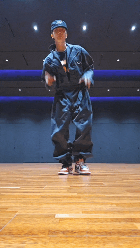 a man in a black jumpsuit and a hat is dancing on a wood floor