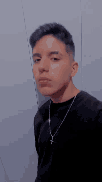 a young man wearing a black shirt and a necklace with a cross on it