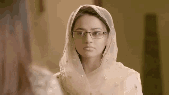 a woman wearing glasses and a head scarf is looking at the camera .