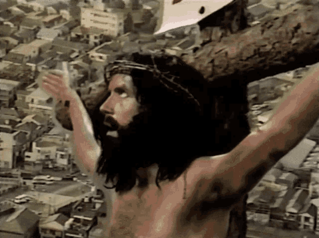 a man with a crown of thorns is carrying a large tree branch