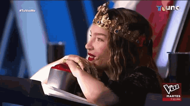 a woman wearing a crown is sitting in front of a tv screen that says " voz " on it