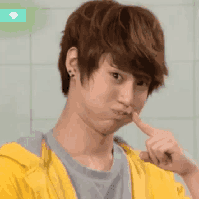 a young man wearing a yellow jacket is making a funny face with his finger in his mouth