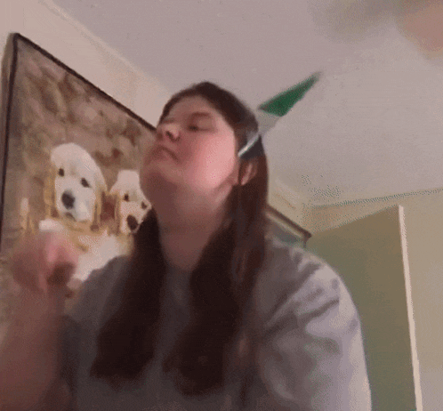 a woman wearing a party hat is standing in front of a painting of three puppies
