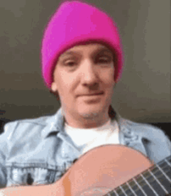 a man wearing a pink hat is playing a guitar .