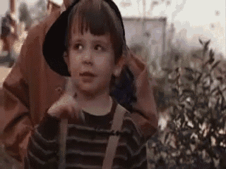 a little boy wearing a hat and suspenders is sitting on a woman 's shoulders .