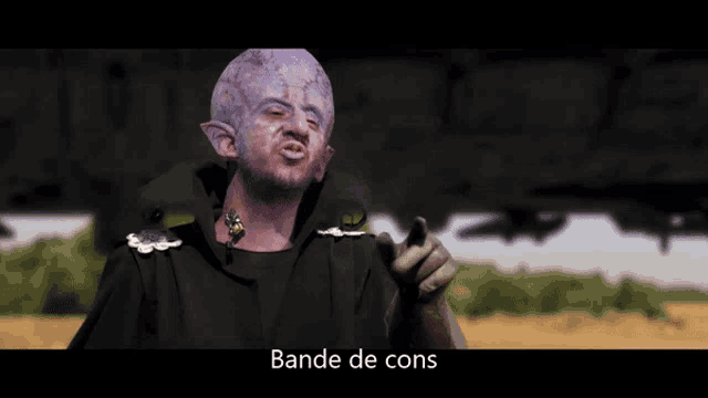 a man with purple paint on his face is pointing and the words bande de cons are below him