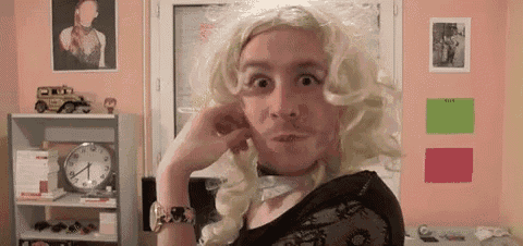 a man wearing a blonde wig and a mustache is making a funny face in a room .