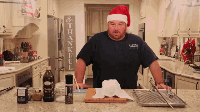 a man wearing a santa hat and an airway shirt stands in a kitchen