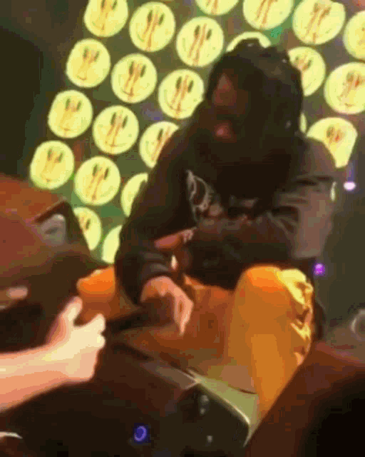 a man in a mask is sitting on a stage with smiley faces on the wall behind him