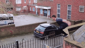 a man is jumping over a car that is parked in front of a building with a sign that says ' ambulance '
