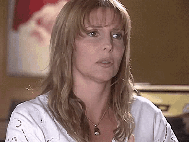 a woman is wearing a white shirt and a necklace with a pendant