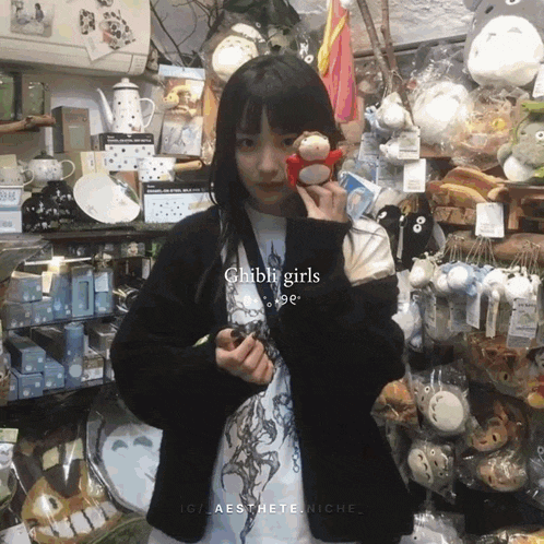 a girl holding a stuffed animal in front of a sign that says ghibli girls on it
