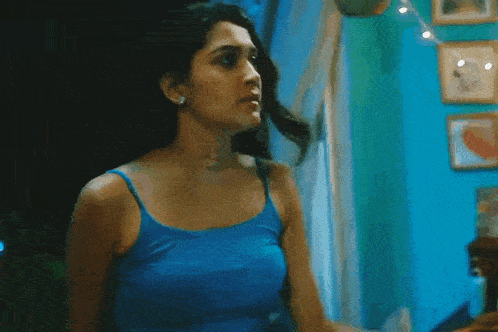 a woman in a blue tank top is standing in a room looking out a window .