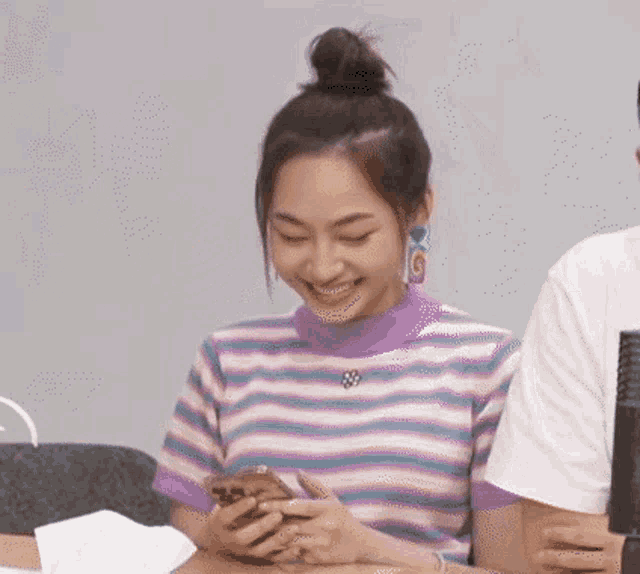 a woman in a striped shirt is sitting at a table looking at her phone .