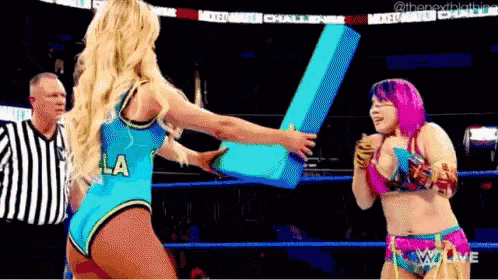 two women are wrestling in a ring and one of them is holding a large blue object .