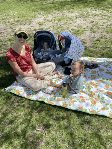 a woman sits on a blanket with a baby in a car seat