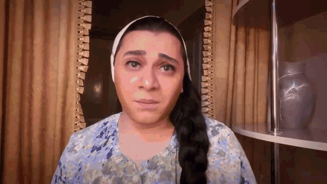 a woman with long hair and a head scarf is making a sad face .