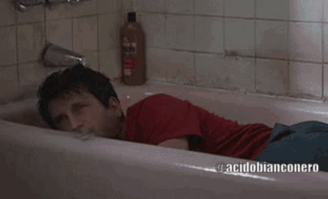 a man in a red shirt laying in a bathtub