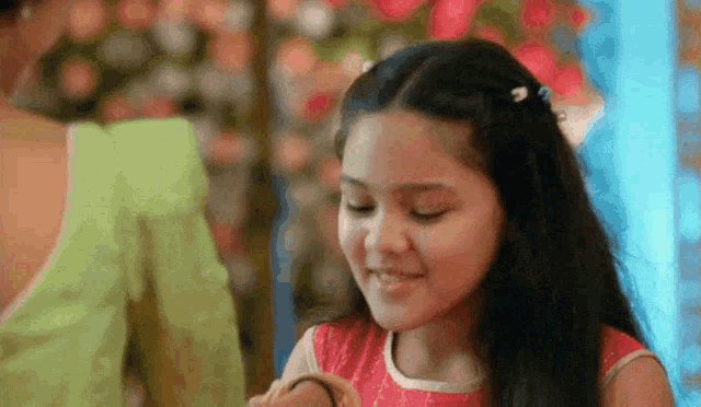 a little girl in a red dress is smiling and holding a bracelet .