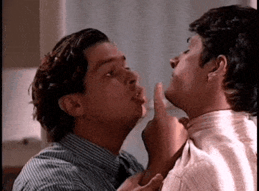 two men are kissing each other on the cheek in a kitchen .