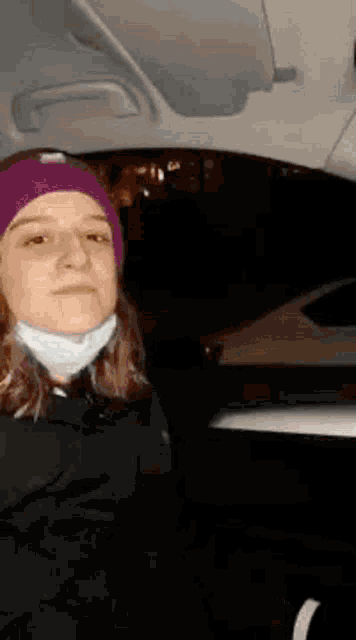 a woman wearing a purple beanie and a mask is sitting in the back seat of a car .