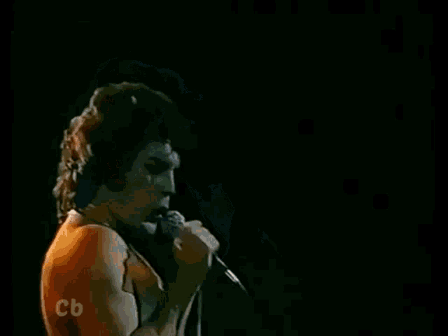 a man is singing into a microphone without a shirt on .